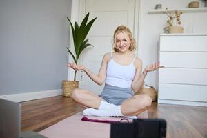 Young female athlete, fitness instructor woman sits on floor rubber mat, recording on digital camera, showing how to workout, explaining exercises photo