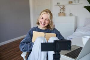 Portrait of cute, smiling young social media content creator, girl records on digital camera and stabiliser, holds notebook, talks to audience, vlogging in her room photo