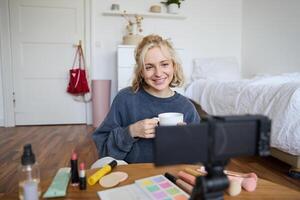 retrato de joven estilo de vida bloguero, mujer sentado en dormitorio y hablando a digital cámara, Bebiendo té, grabación un vlog foto