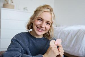 Close up portrait of happy, beautiful young vlogger, content maker recording about makeup, showing beauty products on camera, smiling happily photo