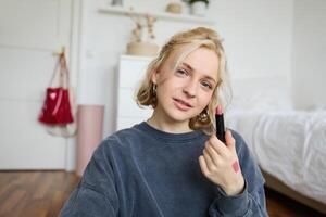 retrato de hermosa joven mujer, contenido creador para social medios de comunicación, sentado en frente de digital cámara, grabación acerca de constituir, demostración lápiz labial muestras en su piel foto