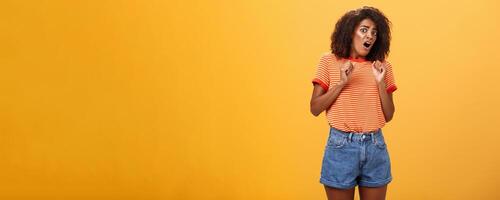 No do not hurt me. Scared silly and insecure good-looking african american woman in stupor screaming for help turning away raising palms near body in defence standing in fright over orange wall photo