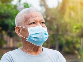 un mayor hombre vistiendo un máscara y mirando arriba mientras en pie en un jardín. máscara para proteger virus, coronavirus, COVID-19, polen granos, y más. concepto de Envejecido personas y cuidado de la salud foto