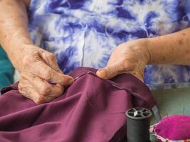 Close-up of hands senior woman's trying to thread a needle for sewing cloth. Space for text. Concept of aged people and relaxation photo