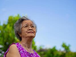 Portrait of an elderly Asian woman wearing glasses and looking up while standing in the garden. Space for text. Concept of aged people, winter season and healthcare photo