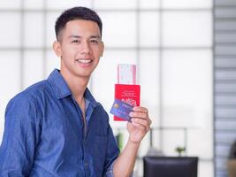 A young man's left hand holding a credit card, passport, smiling, and looking at the camera. Prepare for the upcoming holiday. Holiday concept photo