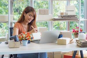 Businesswoman wears casual clothes sitting on a chair in the office. The work desk for an entrepreneur in the office has a laptop, barcode reader, and more. Space for text. Concept of business photo