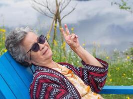 retrato de mayor mujer vistiendo Gafas de sol sentado en silla en el jardín. foto