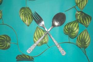 A pair of cutlery set on a turquoise green carpet with foliage decorations photo