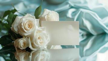 AI generated A bouquet of big and beautiful white roses with an empty white card for writing placed in front of the flowers on shining light-blue silk fabric. Generated by artificial intelligence. photo