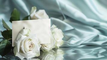 AI generated A bouquet of big and beautiful white roses with an empty white card for writing placed in front of the flowers on shining light-blue silk fabric. Generated by artificial intelligence. photo