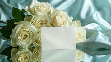 AI generated A bouquet of big and beautiful white roses with an empty white card for writing placed in front of the flowers on shining light-blue silk fabric. Generated by artificial intelligence. photo