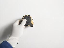 Man's hand with gloves holds a steel measuring tape yellow abnd black color isolated on white background. photo