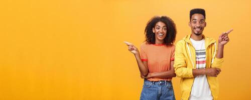 Which one telling true. Joyful and friendly good-looking couple, african american woman pointing left and dark-skinned guy right smiling broadly at camera giving advices but disagree with each other photo