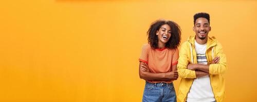 Two african american man and woman being best friends laughing out loud watching funny movie in cinema all dressed up in stylish outfit standing with hands crossed on chest and amused expression photo