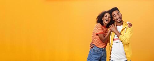 Friends always cover each other. Stylish and carefree loving african american girlfriend hugging boyfriend and smiling broadly touching guy palm hanging around and spending time great together photo