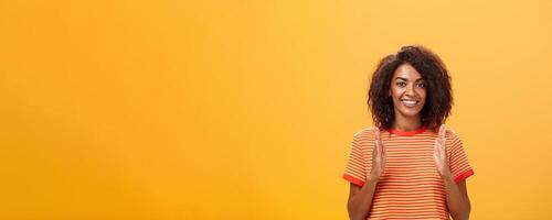 Portrait of charming friendly-looking african american woman with afro hairstyle explaining story with hands and gestures shaping object, holding palms vertical over chest and smiling at camera photo