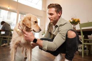 retrato de contento hombre gasto hora con su perro en mascota amigable cafetería, jugando y caricias dorado perdiguero, teniendo divertido, dando él un tratar foto