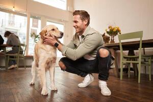 Close up portrait of happy dog owner, man with his pet giving a treat, spending time in animal-friendly cafe or co-working space photo