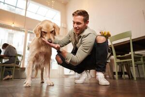 Close up portrait of happy dog owner, man with his pet giving a treat, spending time in animal-friendly cafe or co-working space photo