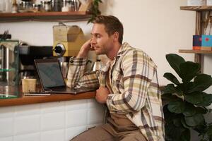 imagen de adulto hombre mirando Complicado a ordenador portátil pantalla, curioso perplejo a su monitor, haciendo difícil tarea en línea, sentado en cafetería, Bebiendo café y trabajando foto