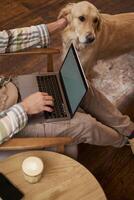 Vertical cropped picture of male hands typing on keyboard, using laptop and petting the dog, cafe visitor working and spending time with his puppy photo