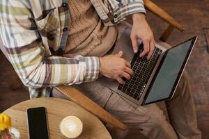 Superior ángulo recortado Disparo de masculino manos, hombre sentado en café con taza de café y trabajando en computadora portátil, mecanografía en teclado, tiene un teléfono en el mesa foto