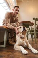 vertical Disparo de joven sonriente hombre con su perro, dorado perdiguero mascota en un café foto