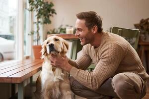 Portrait of happy smiling handsome man, pets his golden retriever and laughs. Young guy with his dog in a cafe photo