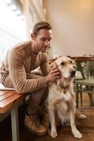 Close up portrait of handsome man with his dog, sitting in cafe. A guy drinks his coffee and touches golden retriever photo