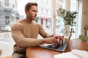 Serious looking cafe owner, handsome man working on laptop, visitor in coffee shop sending an email, typing on his keyboard photo