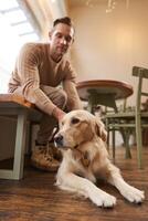 un perro simpático café concepto. hermoso hombre, dorado perdiguero propietario se sienta en un café con su mascota, bebidas café y disfruta el día foto