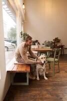 Handsome man sitting in cafe with his dog. A guy drinks coffee and strokes golden retriever. Animal-friendly coffeeshop photo