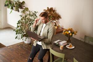 Handsome manager, man in glasses sits on table, holds laptop and types, sends message, works on project, drinks coffee, spends time at co-working space or an office photo