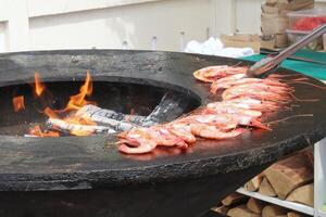 Grilling prawns on brass pan at backyard. Shrimps in frying cast-iron pan in restaurant. Outdoor barbecue cooking. Street food concept. Preparing on stove. Wholesome dish photo