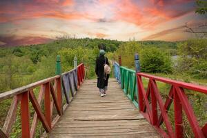 a woman walks across a bridge with a red and green railing. photo