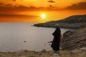 Lonely and sad girl watching sunset by the sea. Longing for the distance and the past. photo