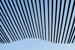 The pattern of the line of tubes sticking out into the sky, black wavy sticks against the background of the blue sky, the minimalistic design of the roof of the house, the abstract decoration photo