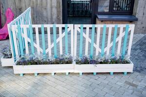 Decorative fence near the entrance to the house, a barrier of boards, wooden pots with flowers, the design of the street space in front of the cafe on the sidewalk. photo