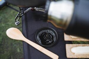 Pour tea from a thermos into a mug, macro photography bubbles of tea foam, a wooden spoon is on the table, breakfast on a hike, tourist dishes, camping. photo