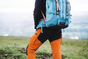 An element of sports equipment is a tourist backpack for hiking in the mountains, a person stands on top of a mountain, a view from behind a tourist in pants, equipment for a hike. photo