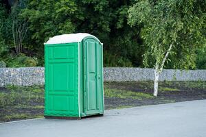 An outdoor bio toilet stands on the sidewalk in a city park, a green plastic toilet, a cabin for wc. photo