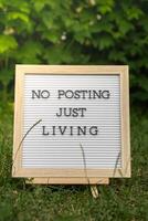 Letter board with text NO POSTING JUST LIVING in grass green background. Concept of digital detox, unplugging from technology break. Mindful living without gadgets photo