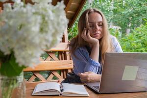 Upset sleepy Female student has online lesson education outdoor in garden wooden alcove. Blonde woman sitting outside work on laptop having call. Unity with nature photo