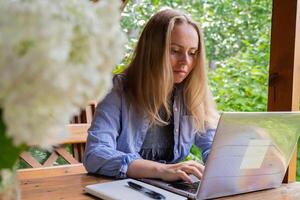 Female student has online lesson education outdoor in garden wooden alcove. Blonde woman sitting outside work on laptop having call. Unity with nature photo