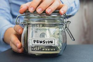 Female hands Saving Money In Glass Jar filled with Dollars banknotes. PENSION transcription in front of jar. Managing personal finances extra income for future insecurity background photo