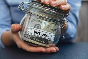 Female hands Saving Money In Glass Jar filled with Dollars banknotes. FUTURE transcription in front of jar. Managing personal finances extra income for future insecurity background photo