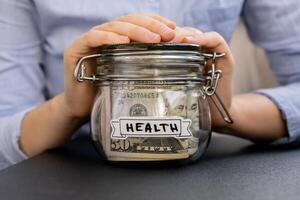 Unrecognizable woman holding Glass jar full of American currency dollars cash banknote with text HEALTH. Preparation saving money. Moderate consumption and economy. Collecting money photo