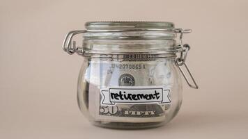 Saving Money In Glass Jar filled with Dollars banknotes. RETIREMENT transcription in front of jar. Managing personal finances extra income for future insecurity. Beige background photo