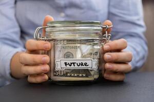 Unrecognizable woman holding Saving Money In Glass Jar filled with Dollars banknotes. FUTURE transcription in front of jar. Managing personal finances extra income for future insecurity background photo